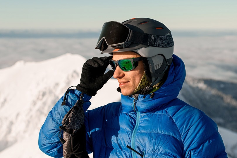 man skier in jacket and helmet on his head straightens his sunglasses