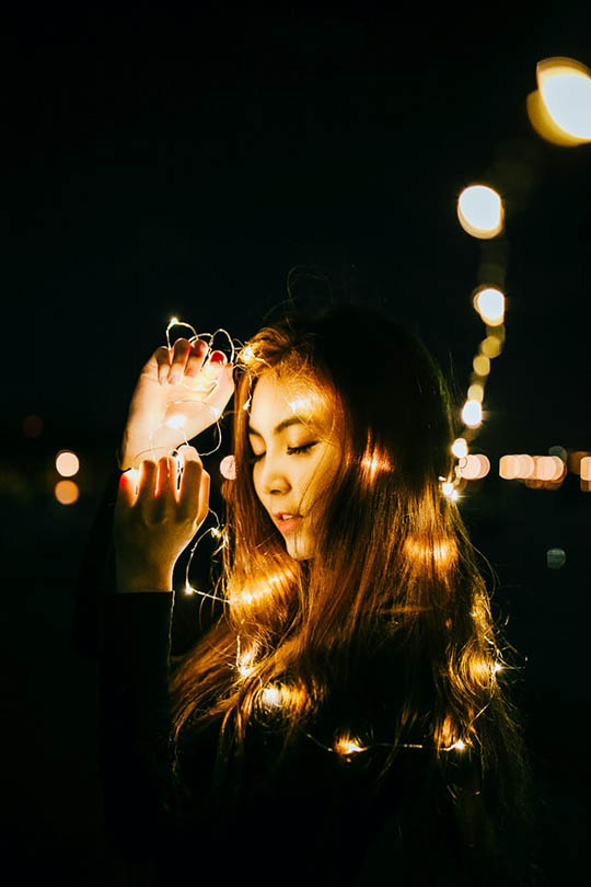 young woman playing fairy lights at night