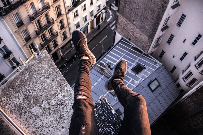 legs and shoes dangling off tall building in city