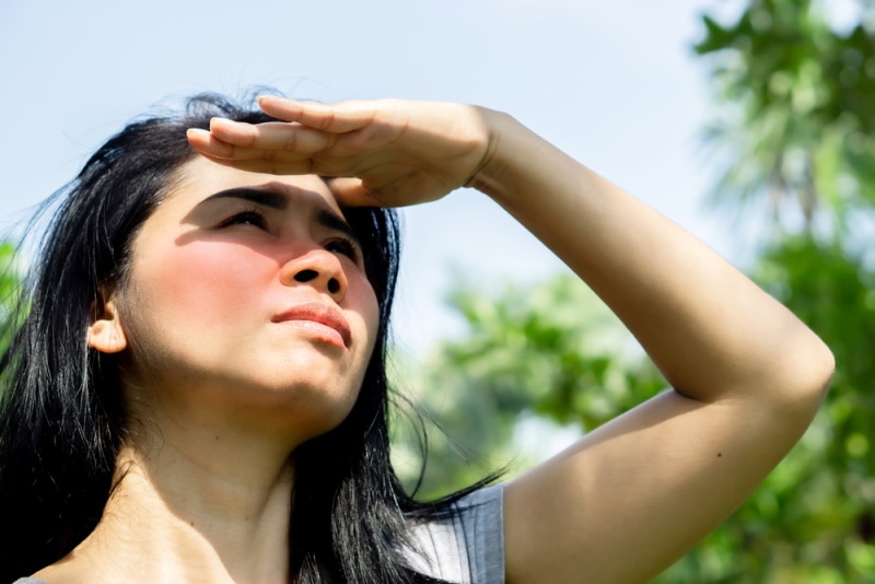 Woman shielding eyes looking at sun with flushed cheeks