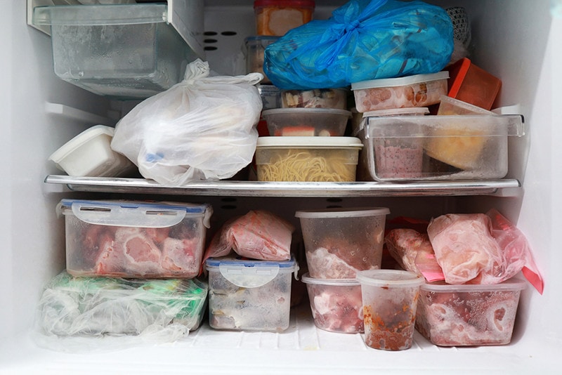 Plastic bags and container with frozen food in freezer refrigerator background