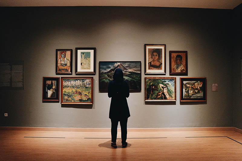 person looking at the paintings on the gallery wall