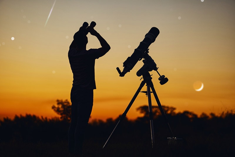 silhouette of a man using binoculars for stargazing